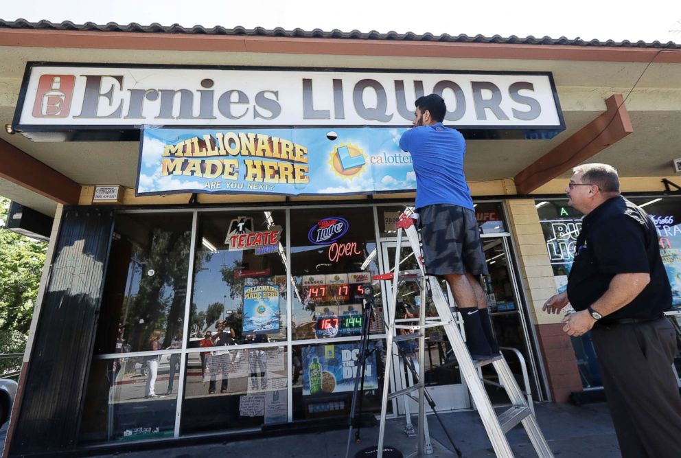 PHOTO: California Lottery official Mike Neis, right, watches as Amol Sachdev hangs a sign over his family's store Ernie's Liquors in San Jose, Calif., July 25, 2018.