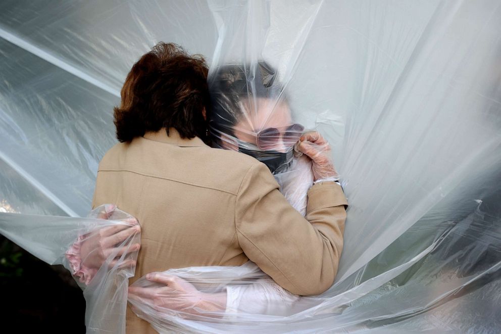 PHOTO: Olivia Grant, right, hugs her grandmother, Mary Grace Sileo through a plastic drop cloth hung up on a homemade clothes line during Memorial Day Weekend on May 24, 2020 in Wantagh, New York.