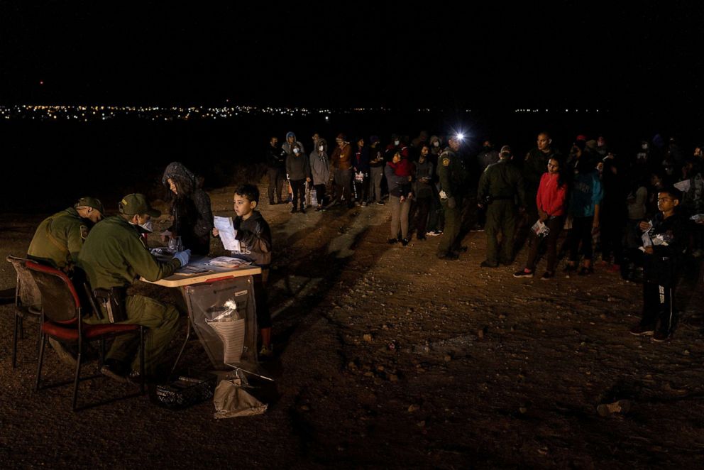 PHOTO: City lights in Mexico are seen in the background as a seven year old unaccompanied migrant boy from Honduras, holds identification paperwork as he is registered by a border patrol agent in Roma, Texas, March 5, 2022.