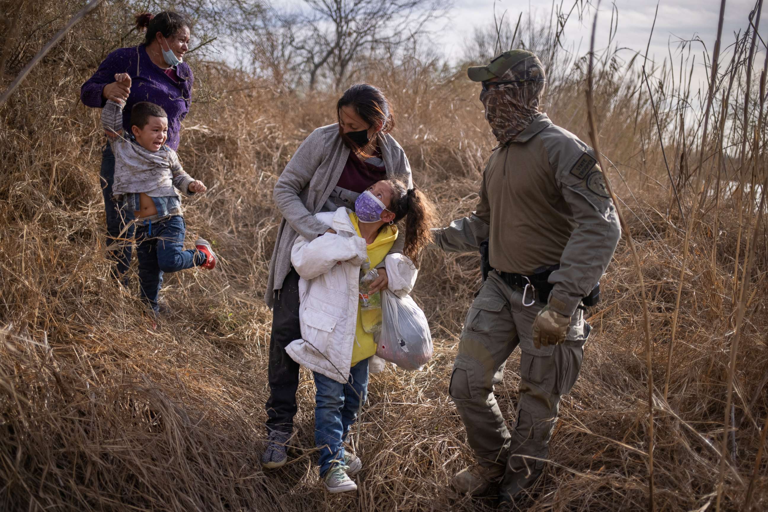 PHOTO: A mother and child from El Salvador and a mother and child from Honduras are escorted out of the brush by a Texas State Trooper after crossing the Rio Grande river into the United States from Mexico on a raft in Penitas, Texas, March 9, 2021.