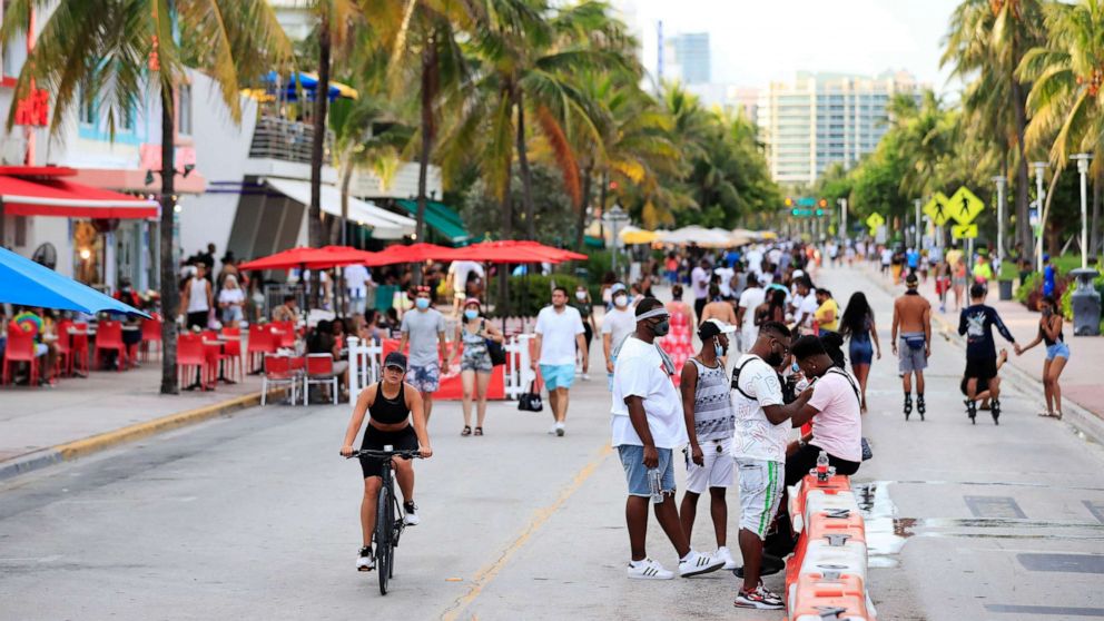 PHOTO: A woman rides her bike past pedestrians on Ocean Drive on July 03, 2020, in the South Beach neighborhood of Miami Beach, Fla.