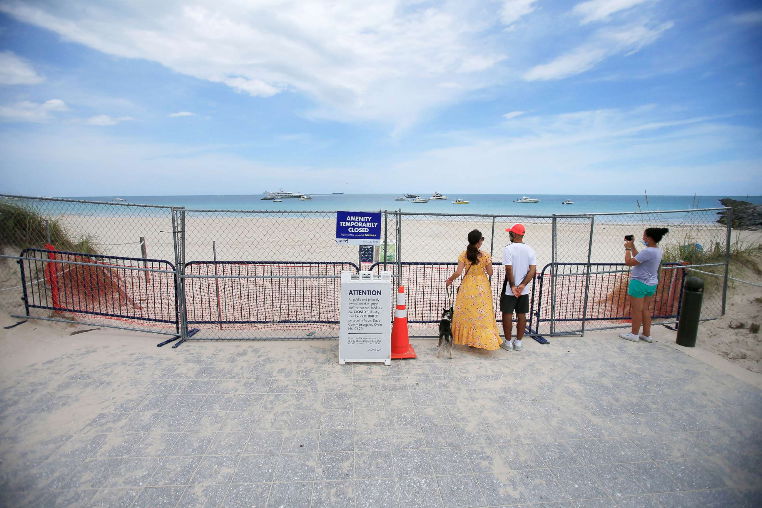 PHOTO: People look through fencing next to signage indicating that the beach is temporarily closed in South Pointe park, July 4, 2020, in the South Beach neighborhood of Miami Beach, Fla.