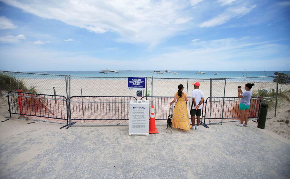 PHOTO: People look through fencing next to signage indicating that the beach is temporarily closed in South Pointe park, July 4, 2020, in the South Beach neighborhood of Miami Beach, Fla.