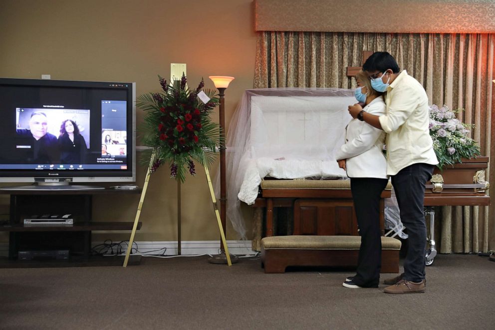PHOTO: German Amaya Jr., hugs his mother Glena Amaya as they mourn during the wake for his father, German Amaya, as a screen broadcasts services via Zoom with family and friends on Aug. 08, 2020, in Miami. German Amaya died from COVID-19.
