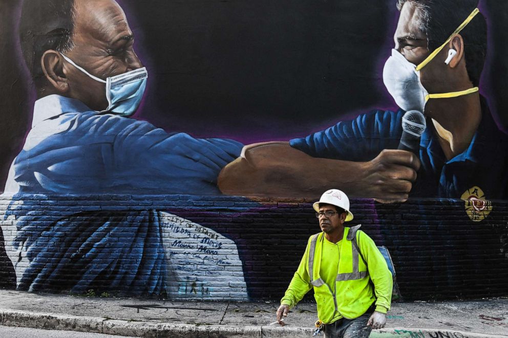 PHOTO: In this file photo a construction worker walks past a mural by Hiero Veiga of Moishe Mana, left, and Miami Mayor Francis X. Suarez wearing masks in Wynwood Art District in Miami, Florida on June 29, 2020.