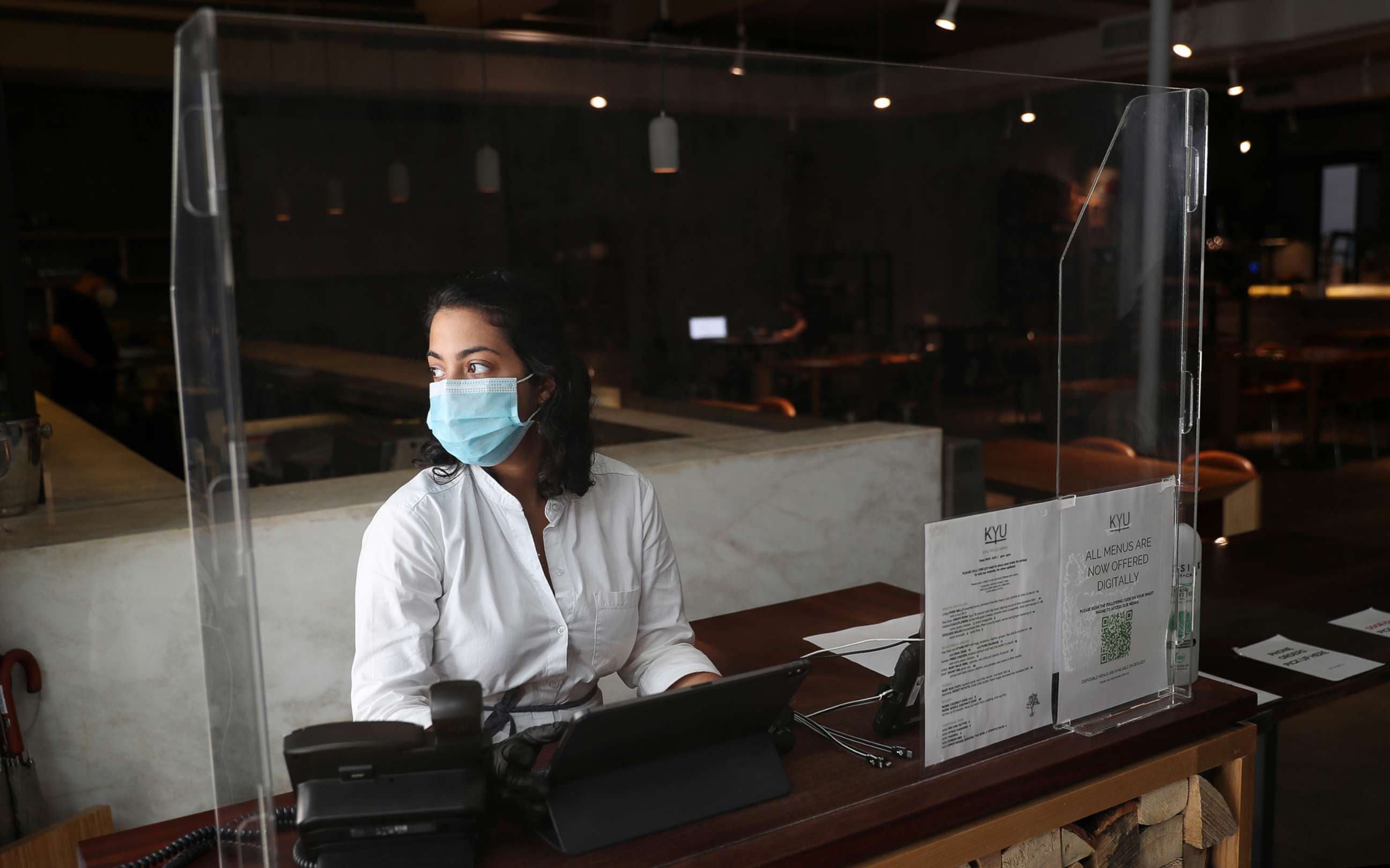 PHOTO: Hostess Ashley Clinton waits for customers behind a plexiglass partition at the KYU restaurant, July 9, 2020 in Miami.