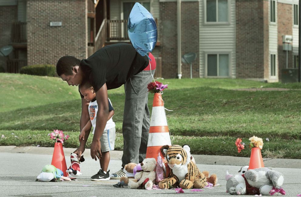 PHOTO: Canfield Green Apartments resident Marcus Hill helps his son Messiah Hill, 2, place a stuffed animal at a newly rebuilt memorial to Michael Brown, Jr. on Thursday, Aug. 8, 2019, in Ferguson, Mo.