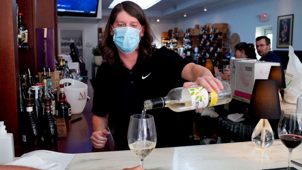 PHOTO: A bartender wears a mask as he pours a glass of wine for a customer at Cork on Saginaw, which reopened fully for the first time amidst COVID-19 on June 8, 2020, in downtown Flint, Mich.