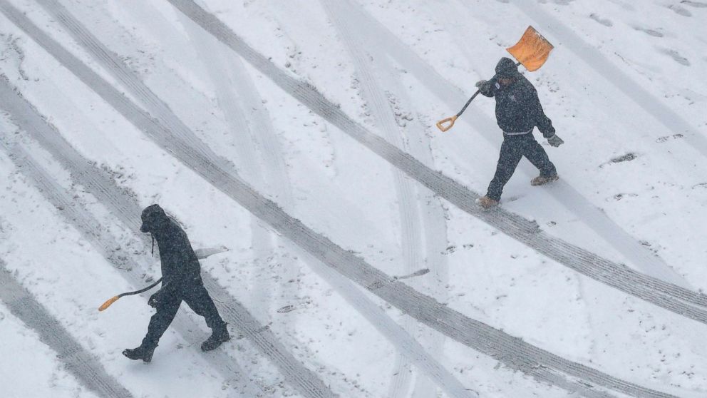 Workers carry snow shovels as snow falls, Nov. 25, 2018, in downtown Kansas City, Mo.