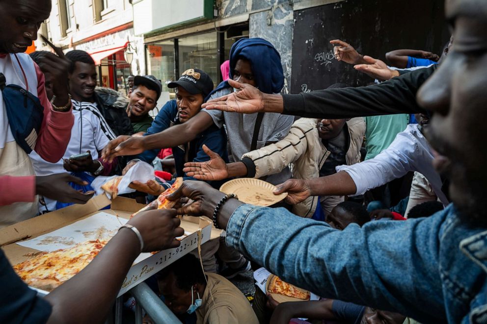 PHOTO: A police officer hands out pizza to dozens of recently arrived migrants to New York City as they camp outside of the Roosevelt Hotel, which has been made into a reception center, where they try to secure temporary housing on Aug. 01, 2023.