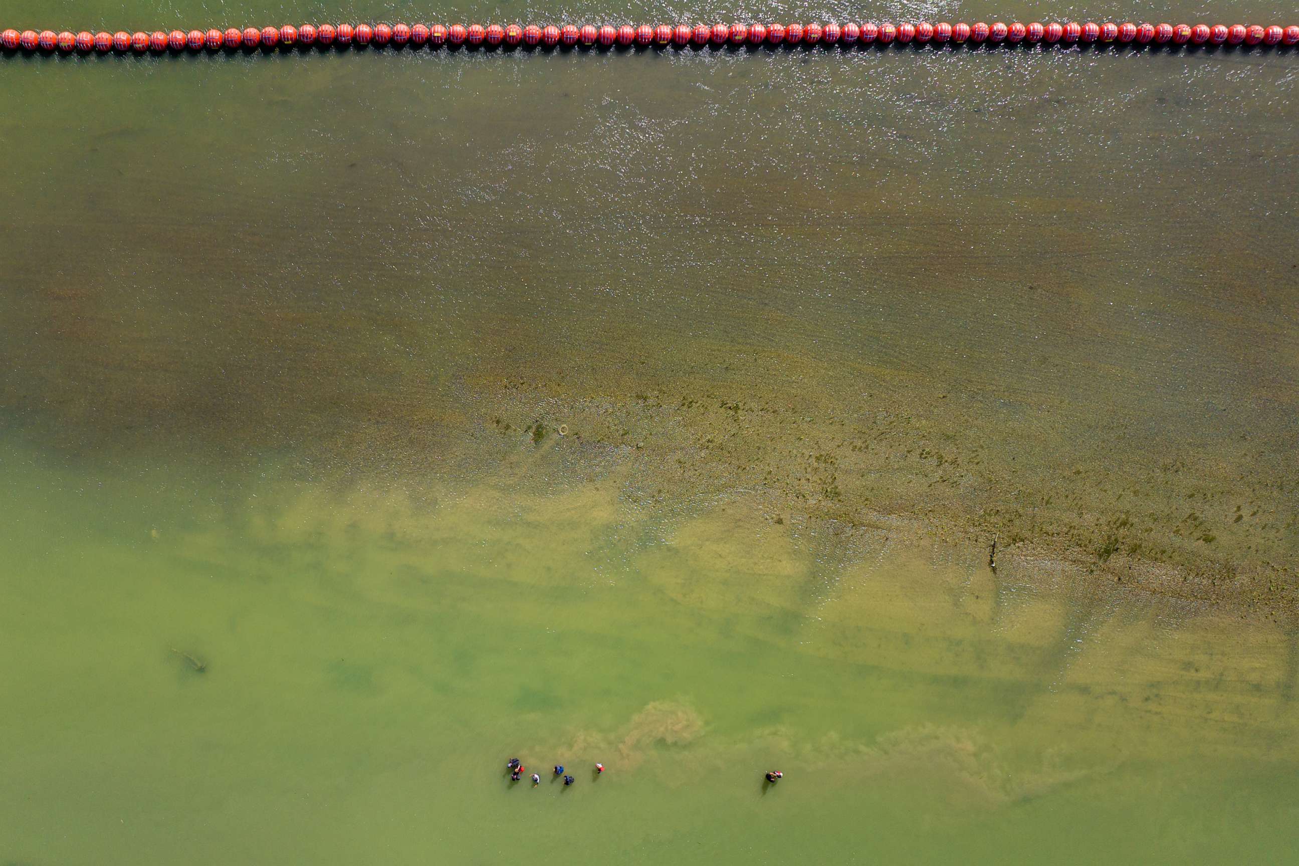 PHOTO: In an aerial view, migrants seeking asylum walk alongside buoy barriers in an attempt to cross the Rio Grande river into the United States in Eagle Pass, Texas, on July 18, 2023.