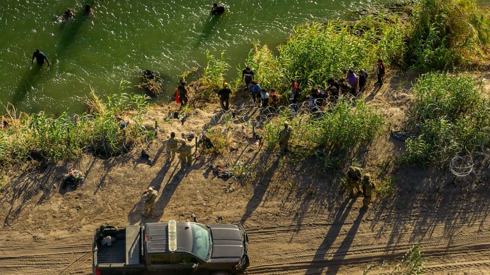 PHOTO: In an aerial view, migrants seeking asylum receive instructions from law enforcement officers in Eagle Pass, Texas, after crossing the Rio Grande river into the United States on July 18, 2023.