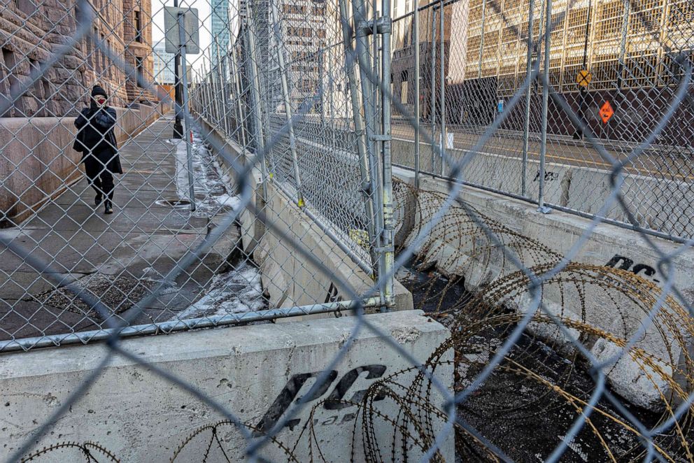 PHOTO: A woman walks past layers of barbed wire fence and razor wire in front of the Hennepin County Government Headquarters in Minneapolis, March 3, 2021.