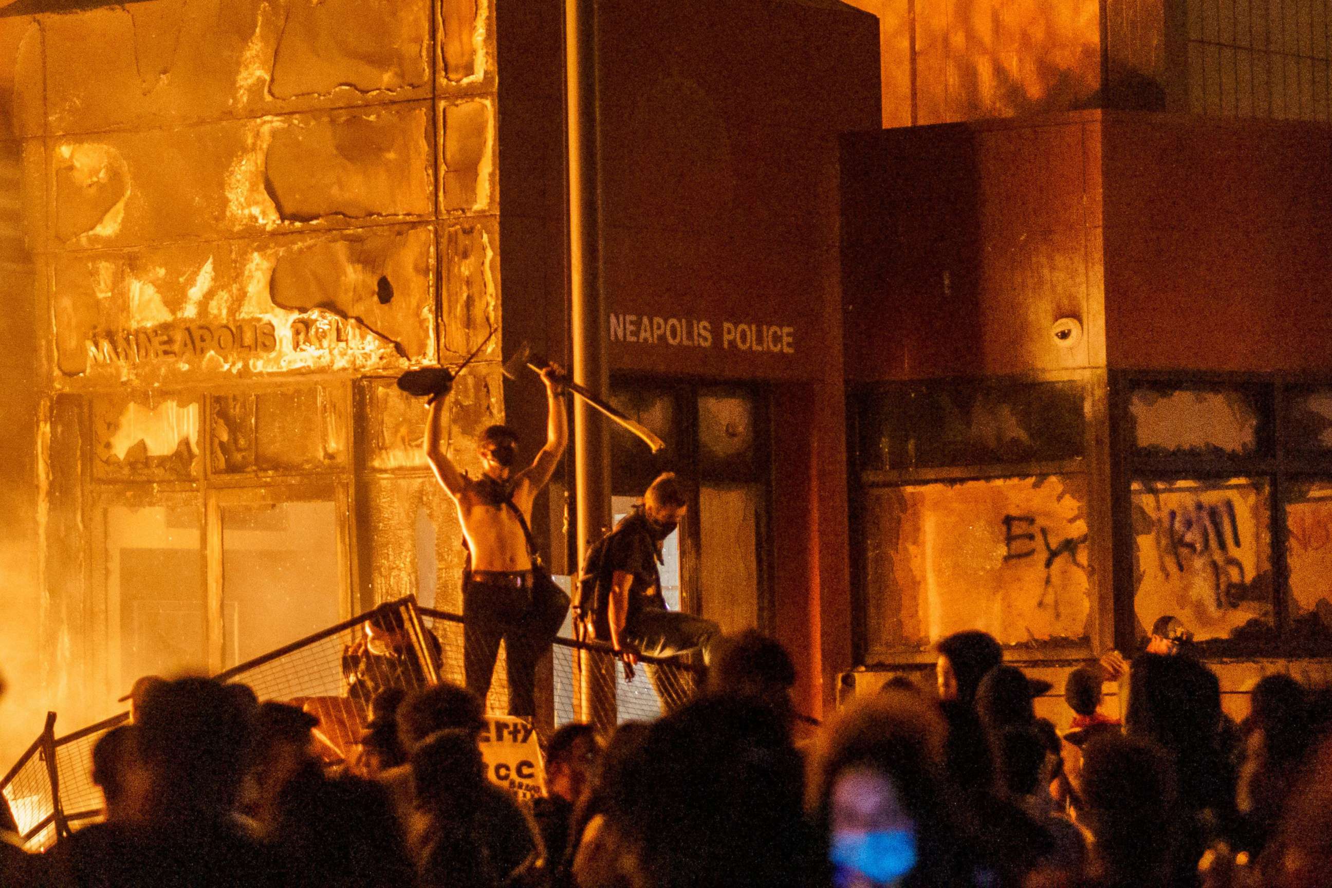 PHOTO: In this May 28, 2020, file photo, flames from a nearby fire illuminate protesters standing on a  barricade in front of the Third Police Precinct in Minneapolis.