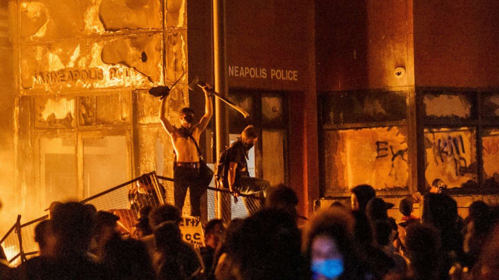 PHOTO: In this May 28, 2020, file photo, flames from a nearby fire illuminate protesters standing on a  barricade in front of the Third Police Precinct in Minneapolis.