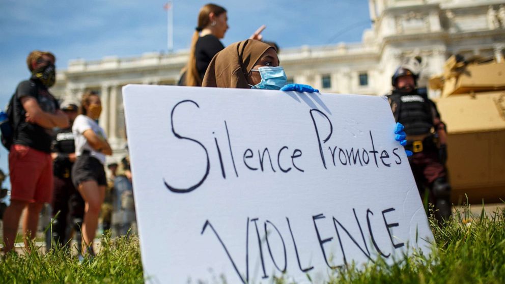 PHOTO: A demonstrator sits by her sign reading "Silence Promotes Violence" outside of the state capital building guarded by National Guards and State Patrol, May 31, 2020 in Saint Paul, Minnesota.