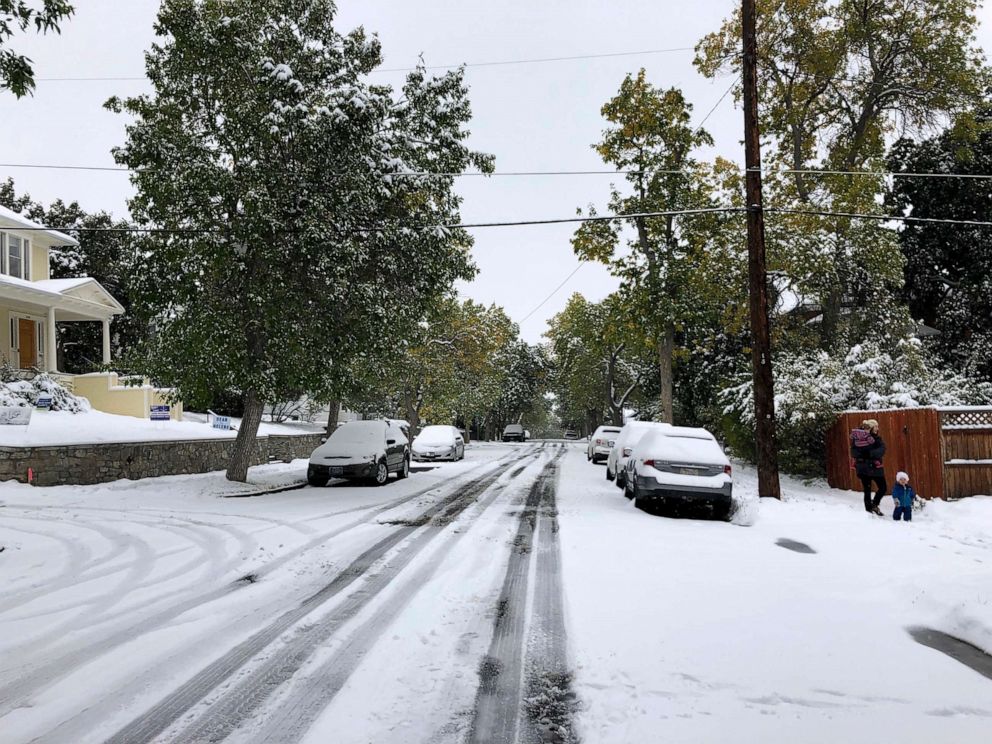 PHOTO: Pedestrians make their way along a snow covered street lined with trees that still have their leaves during a fall snowstorm in Helena, Mont., Sept. 29, 2019. 