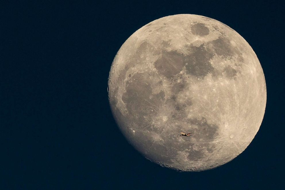 PHOTO: A plane flies past the moon at sunset on March 3, 2015 in London.