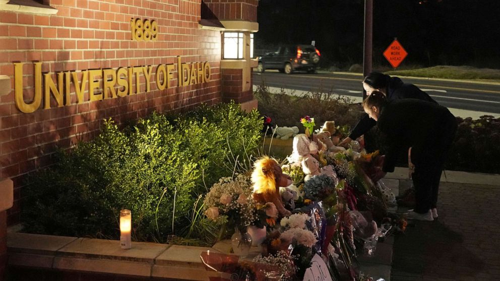 PHOTO: Two people place flowers at a growing monument in front of a University of Idaho campus entrance sign on November 16, 2022 in Moscow, Idaho. 