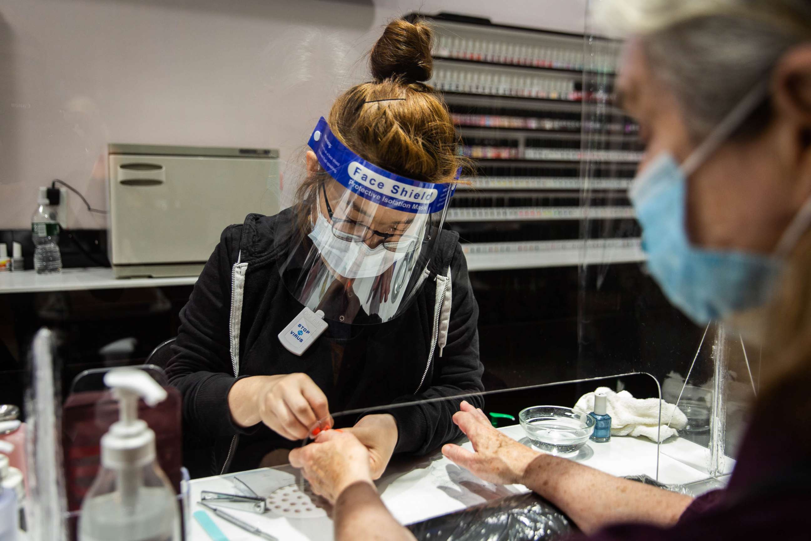 PHOTO: A worker wearing a protective mask and face shield gives a customer a manicure behind a plastic barrier at a nail salon in Syracuse, New York, June 15, 2020.