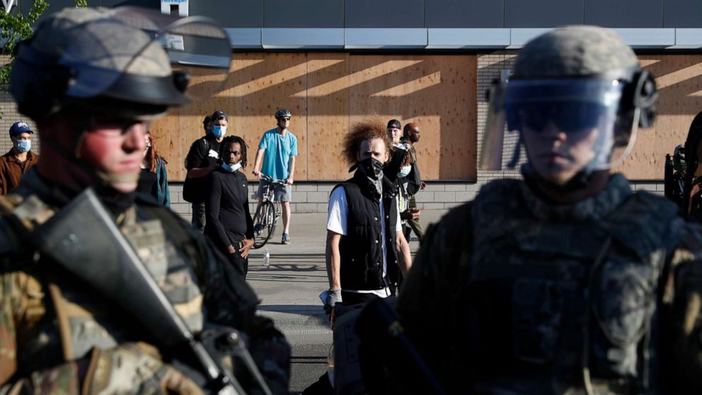 PHOTO: Demonstrators gathered near members of the Minnesota National Guard walk past onlookers Friday, May 29, 2020, in Minneapolis.