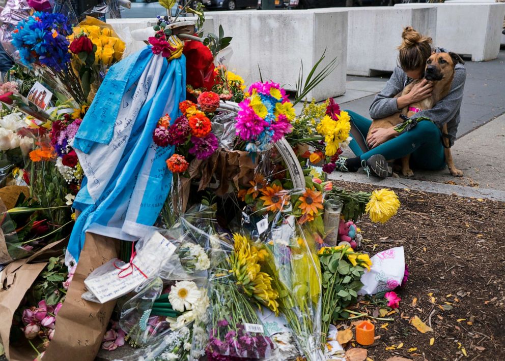 A woman hugs her dog after placing flowers she brought to a makeshift memorial that honors victims of an attack who were struck and killed by a rental truck driven by Sayfullo Saipov at Chambers and West Streets in New York, Nov. 4, 2017.