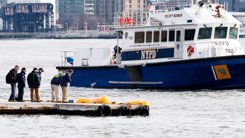 PHOTO: NTSB investigators and a New York City police boat gather near yellow flotation devices attached to the skids of a submerged sightseeing helicopter that crashed a night earlier on the East River in New York, March 12, 2018.