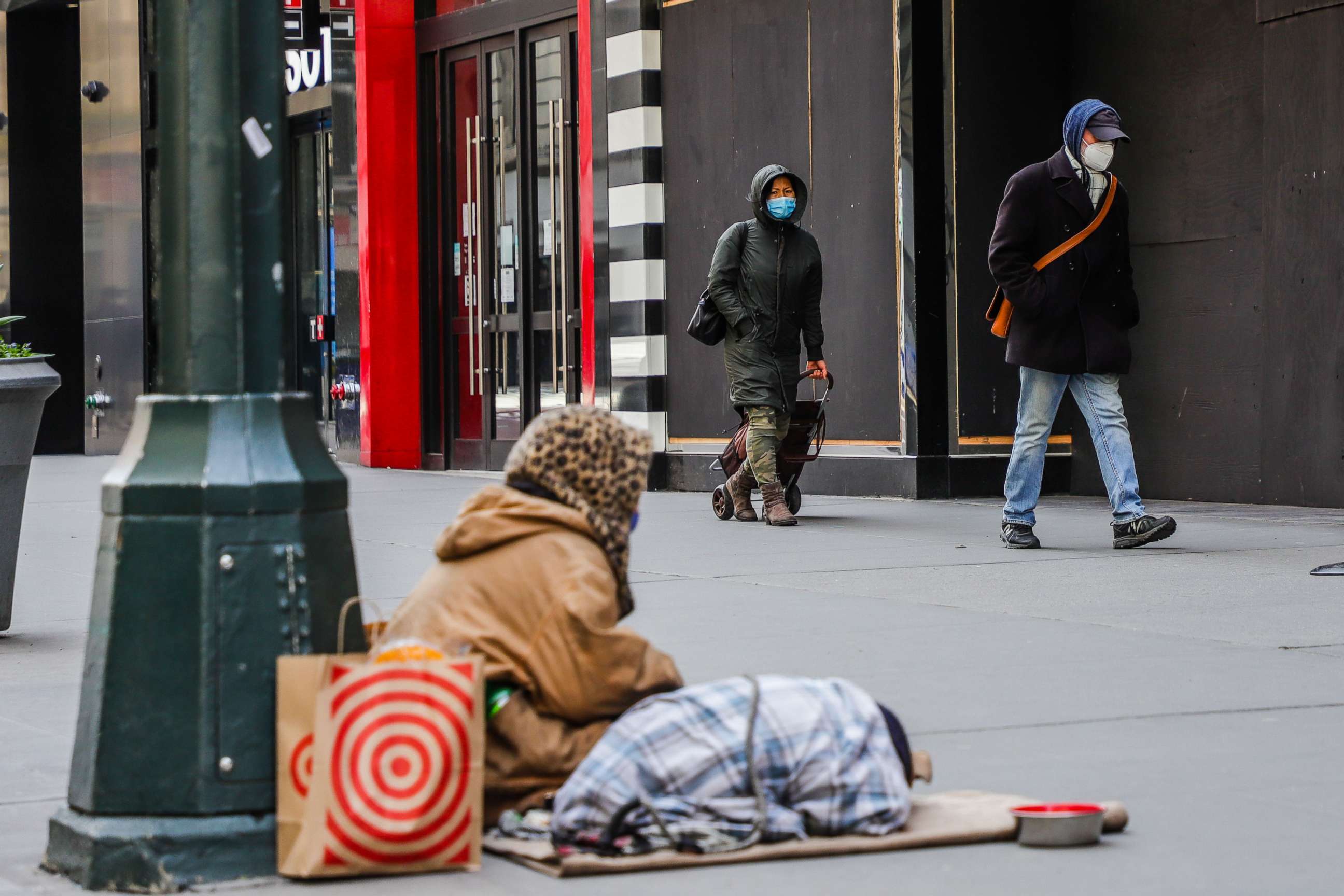 PHOTO: People wearing masks walk in front of a homeless person in New York during the COVID-19 coronavirus pandemic, April 17, 2020.