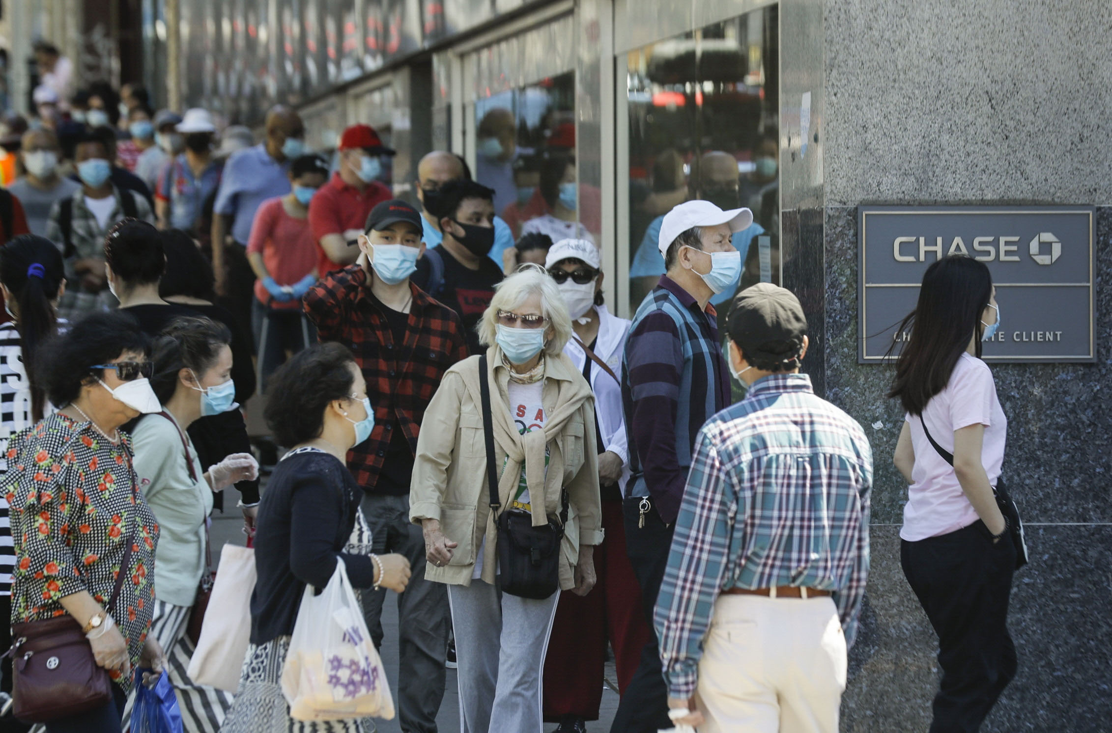 PHOTO: Patrons wearing protective masks wait to enter a Chase bank location, June 8, 2020, in the Queens borough of New York. After three bleak months, New York City will try to turn a page and begin reopening Monday after getting hit by the coronavirus.