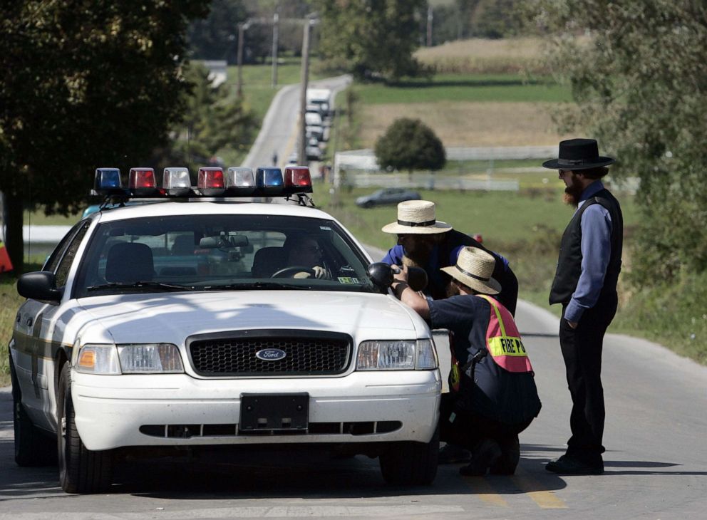 PHOTO: Amish men speak with a police officer on a road leading to the one-room West Nickel Mines Amish School, Oct. 3, 2006, in the town of Nickel Mines, Penn. a day after a shooting at the school left three girls dead.