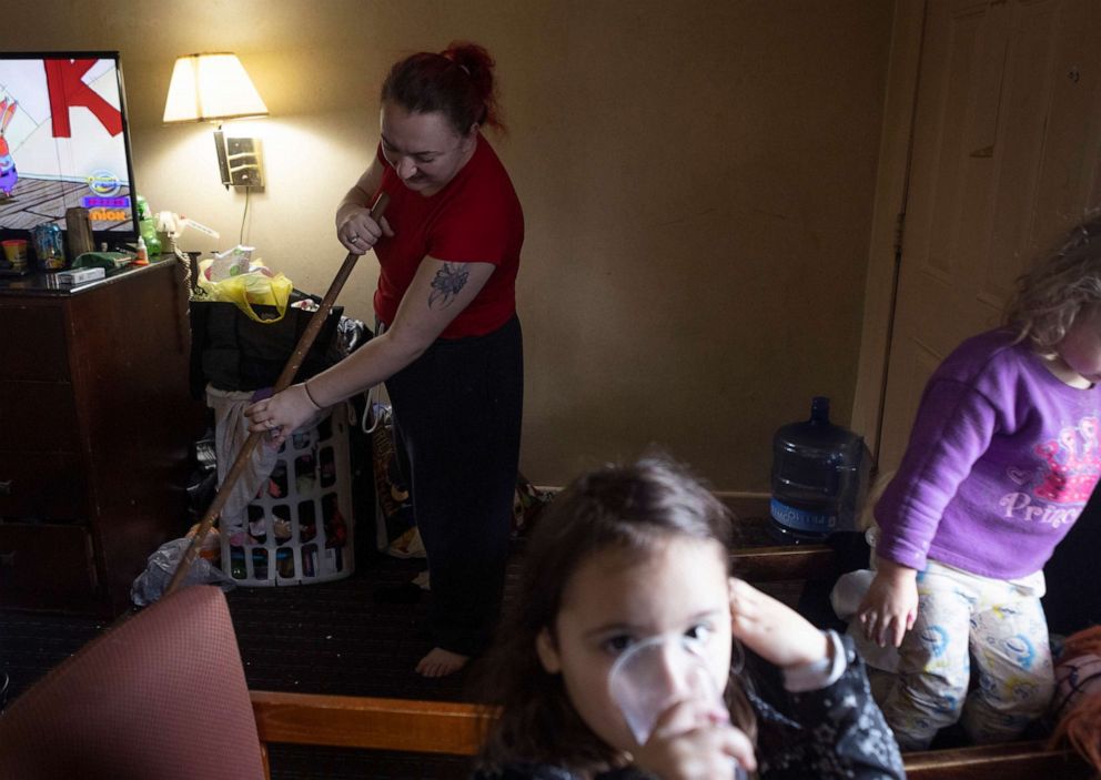 PHOTO: Nicki Schools sweeps the floor while she watches her daughter NyAnna, center, and Audrey, a girl she babysits five days a week, Jan. 6, 2022 in Richmond, Va.