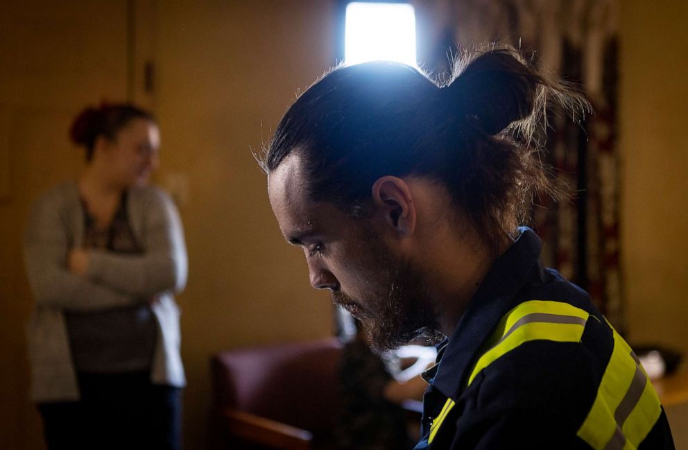 PHOTO: Brian House rests in his motel room after work while his partner, Nicki Schools stands near the door, Jan. 10, 2022, in Richmond, Va. Brian and Nicki are working to save enough money for rent and utilities deposits to move into their own apartment.