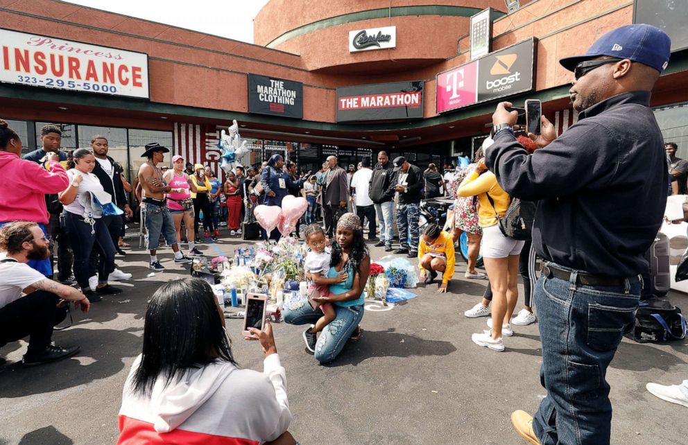 PHOTO: Mourners and supporters take photos as they gather at a growing memorial in front of The Marathon Clothing store, April 1, 2019, in Los Angeles, where rapper Nipsey Hussle was killed and two others wounded outside his store the day prior.