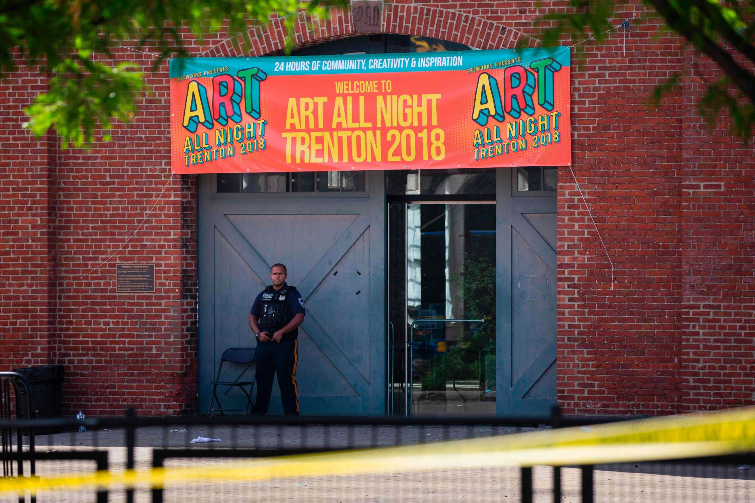PHOTO: A Police officer stands in front as other officers inspect the crime scene at the Roebling Market, June 17, 2018, the morning after a shooting at an all-night art festival injured 20 people and left one person dead in Trenton, New Jersey.