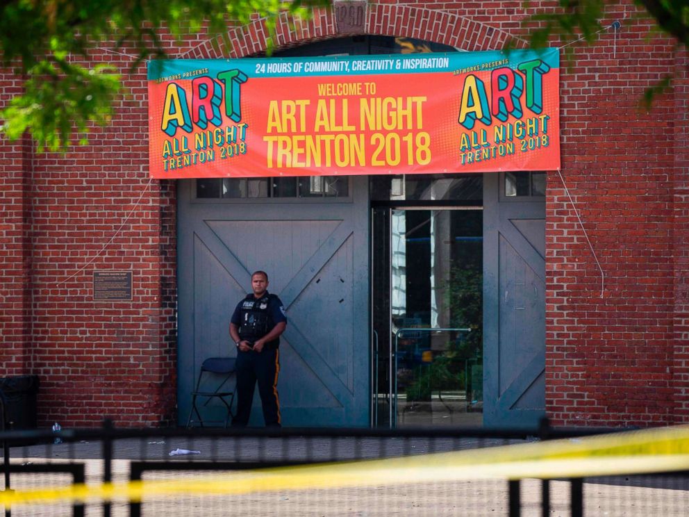 PHOTO: A Police officer stands in front as other officers inspect the crime scene at the Roebling Market, June 17, 2018, the morning after a shooting at an all-night art festival injured 20 people and left one person dead in Trenton, New Jersey.