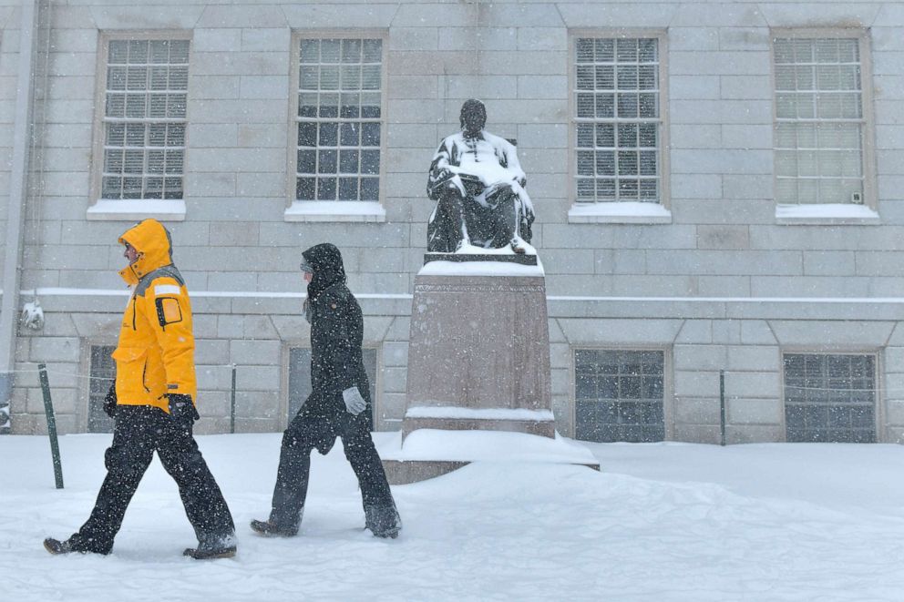 PHOTO: A pair of pedestrians walk past the statue of John Harvard in Harvard Yard, during a storm that was projected to bring up to two feet of snow to the region, Jan. 29, 2022, in Cambridge, Mass. 