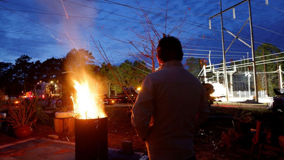 PHOTO: Gerardo Anicero warms in front of a makeshift fire as he watches Duke Energy crews work to restore power at a crippled electrical substation in Carthage, NC, on Dec. 4, 2022. 