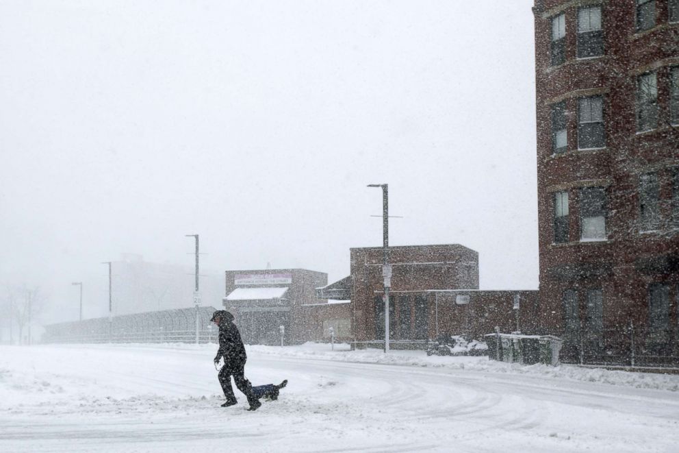 PHOTO: A man crosses a street with his dog against heavy winds and blowing snow as a winter storm bears down, March 13, 2018, in Boston.