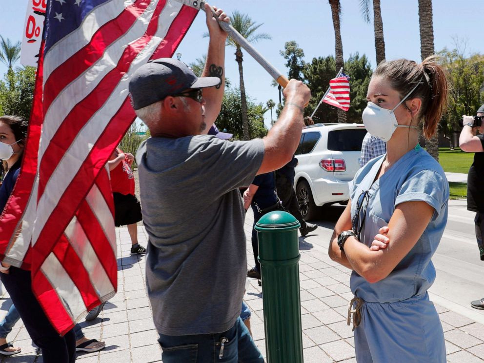 PHOTO: A health care worker stands in counter protest as people march towards the Arizona State Capitol in protest of Gov. Doug Ducey's stay-at-home order to combat the coronavirus in Phoenix, April 20, 2020. 