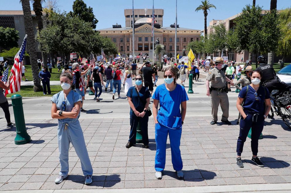 PHOTO: Health care workers stands in counter protest as people march towards the Arizona State Capitol in protest of Gov. Doug Ducey's stay-at-home order to combat the coronavirus, April 20, 2020., in Phoenix.