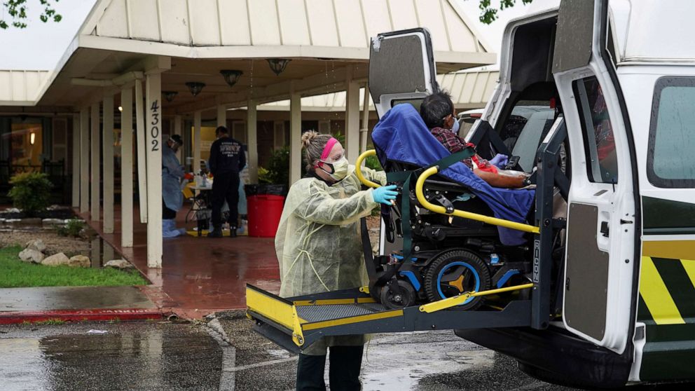 PHOTO: A healthcare worker in a protective suits helps an elderly person to get off an ambulance on April 4, 2020.