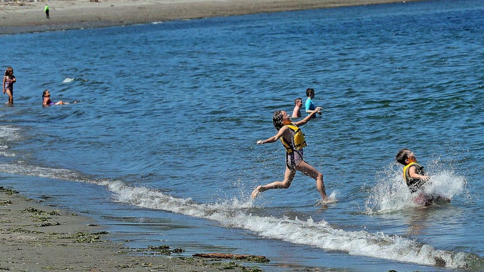 PHOTO: Siblings Athena and Aremis Shepard run into the water at in Hansville, Wa., as temperatures began to climb in the Northwest, July 25, 2022.