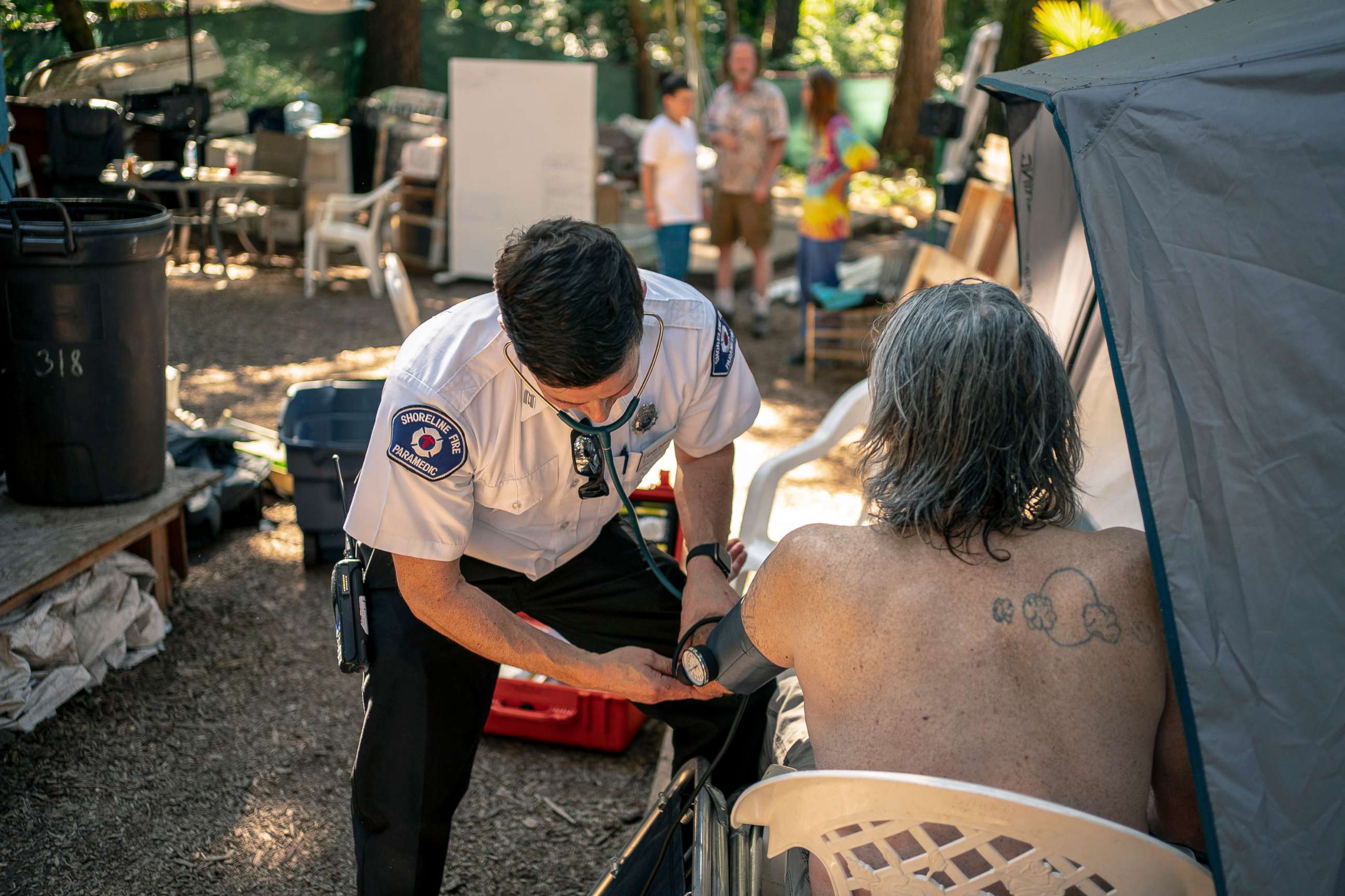 PHOTO: Gabe DeBay, Medical Services Officer with the Shoreline Fire Department, checks the blood pressure of a homeless man at a tent encampment during the hottest part of the day, July 26, 2022, in Shoreline, Wa.