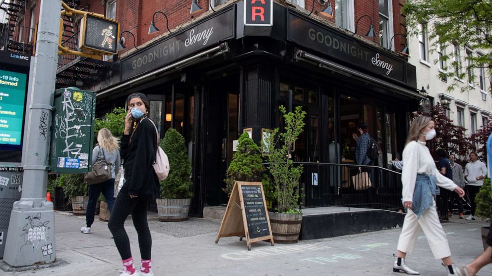 PHOTO: People wearing masks walk past an recently reopened bar in the East Village amid the coronavirus pandemic, May 14, 2020, in New York City.