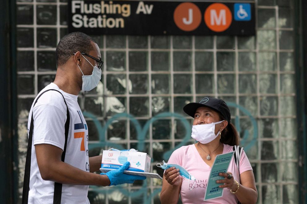 PHOTO: Stephane Labossiere, left, with the Mayor's Office of Immigrant Affairs, hands out masks and printed information about free COVID-19 testing in Brooklyn being offered by NYC Health + Hospitals, Wednesday, July 8, 2020, in New York.