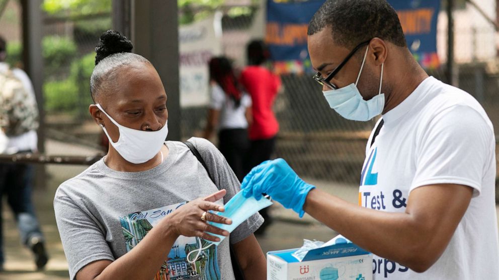 PHOTO: Stephane Labossiere, right, with the Mayor's Office of Immigrant Affairs, hands out masks and printed information about free COVID-19 testing in Brooklyn being offered by NYC Health + Hospitals, Wednesday, July 8, 2020, in New York.