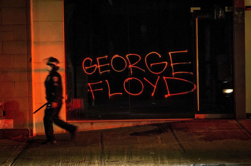 PHOTO: A New York Police Department (NYPD) officer wields a baton as he walks by a graffiti reading the name 'George Floyd' during a protest in New York City, May 31, 2020, during protests.