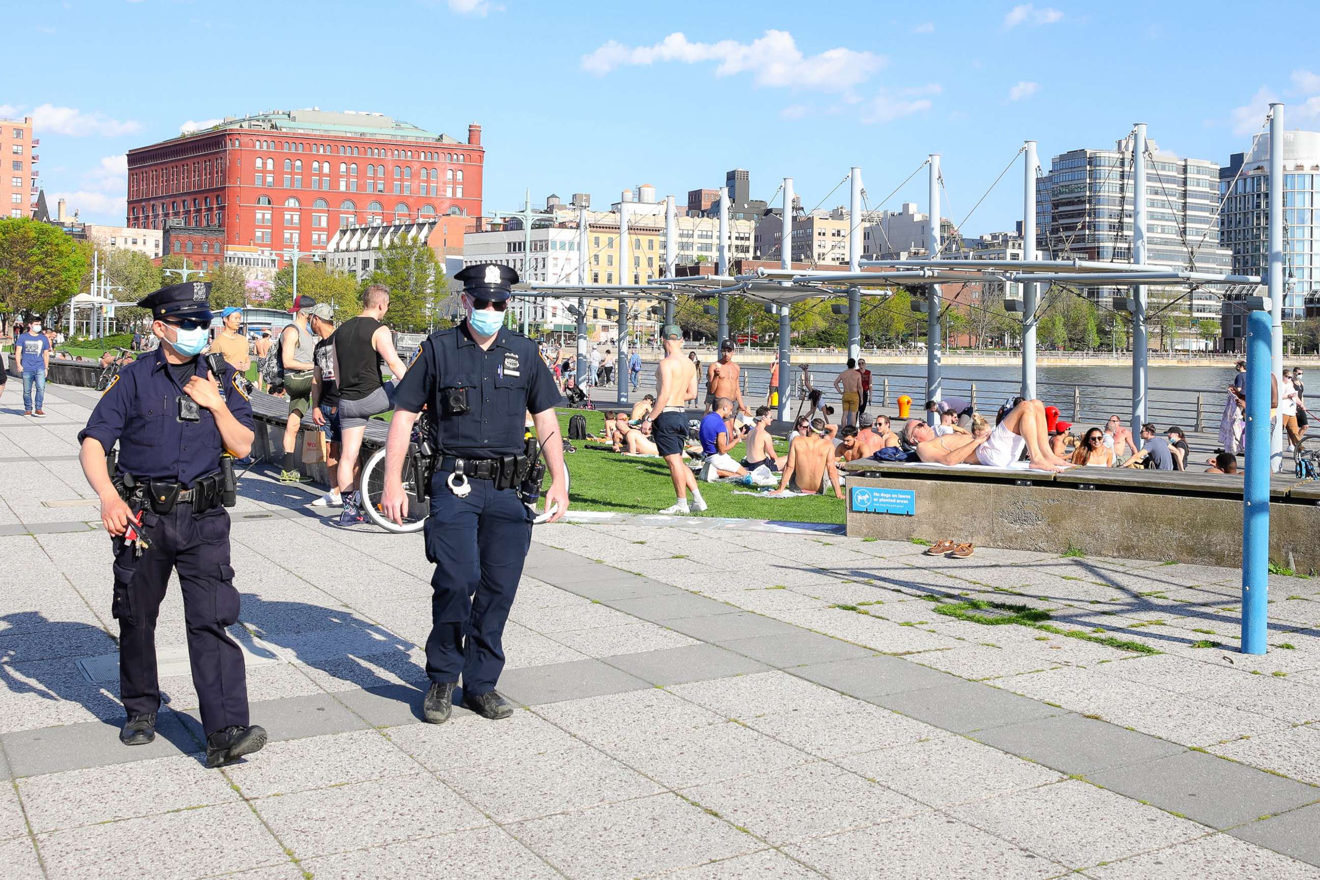 PHOTO: NYPD officers walk by people enjoying the warmer temperatures along the Hudson River on May 03, 2020, in New York.