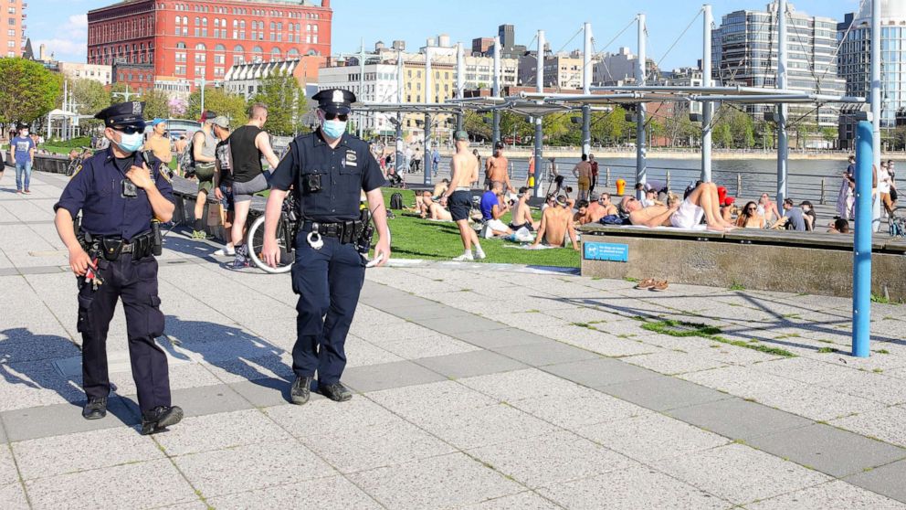 PHOTO: NYPD officers walk by people enjoying the warmer temperatures along the Hudson River on May 03, 2020, in New York.