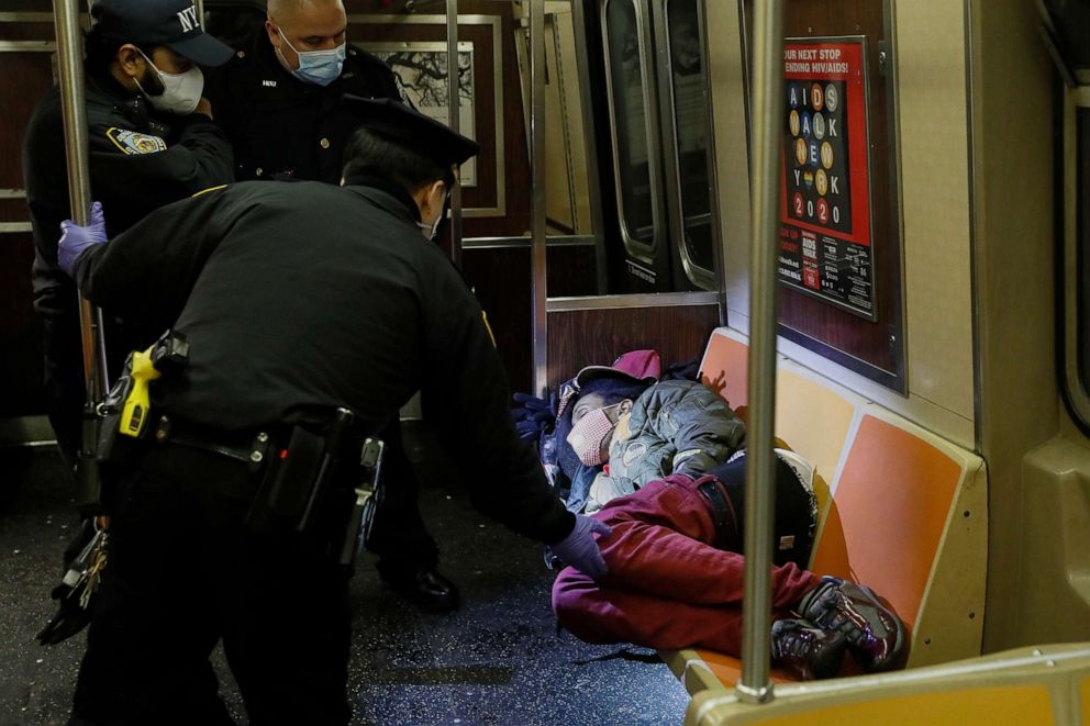 PHOTO: NYPD and MTA officers wake up a sleeping passenger before directing him to exit the 207th Street A-train station, April 30, 2020, in the New York.